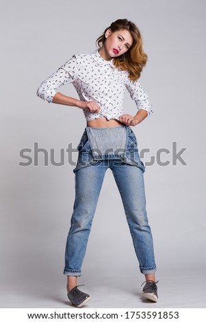 High fashion photo of a beautiful elegant young woman in a pretty denim jeans jumpsuit, shirt, hairstyle on white, soft gray background. Studio Shot. 