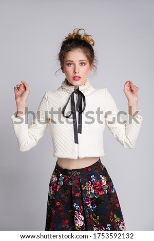 High fashion photo of a beautiful elegant young woman in a pretty dark long skirt with floral pattern, leather jacket on white, soft gray background. Studio Shot. 