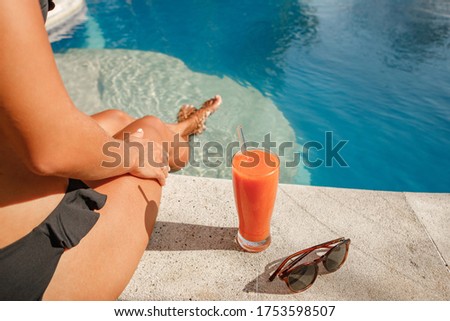 Beautiful woman good shape leg sit tnear  swimming pool. Drink orange juice on happy holiday. orange juice and sunglasses by the pool