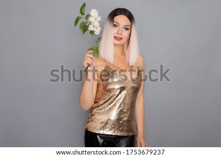 Young stylish blonde woman dressed in a golden top holds in her hands a branch of a white lilac. studio shot