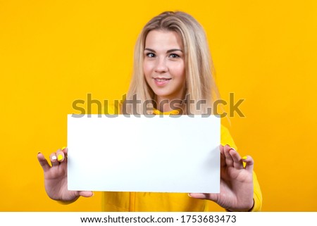 Your text here. Beautiful young caucasian woman holding empty blank board for advertising. Studio portrait of sporty cute girl on yellow background.