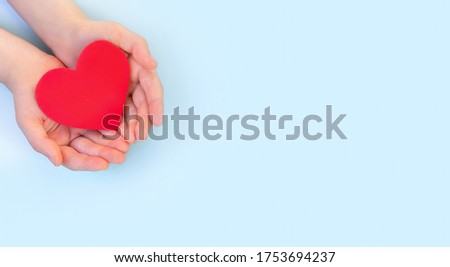 Children's hands hold red heart on a light background. Concept health care, organ donation, wellbeing.World health day.Banner