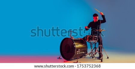 Caucasian male drummer improvising isolated on blue studio background in neon light. Performing, looks inspired, energy. Concept of human emotions, facial expression, ad, music, art, festival. Flyer. Royalty-Free Stock Photo #1753752368
