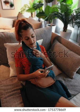 Woman sitting on the sofa at home chatting with her cell phone during the quarantine due to the coronavirus