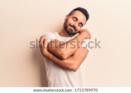 Young hispanic man wearing casual clothes hugging oneself happy and positive, smiling confident. self love and self care  Royalty-Free Stock Photo #1753789970