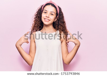 Beautiful kid girl with curly hair wearing casual clothes looking confident with smile on face, pointing oneself with fingers proud and happy. 