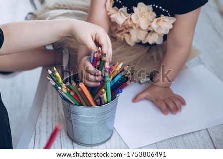 Children's hands reach for an iron vase with colored pencils