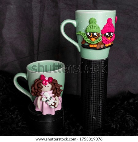 The original mug with decorative figurines made with their own hands. A lovely birthday present. Figures on the cup are fashioned hand made from colored clay. Dark background. High quality photo