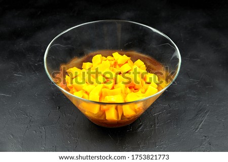 Pumpkin pieces in a deep transparent glass bowl on black table. Chopped pumpkin (butternut squash) in salad dish. Cooking vegetable food