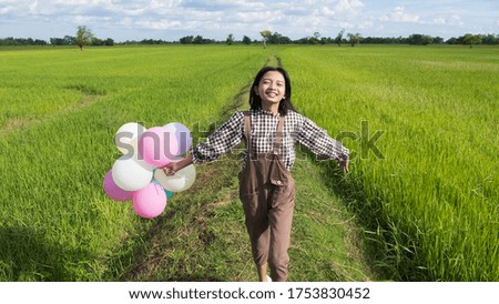 Happy Asian young girl holding balloon running at beautiful field rice, Nature background.