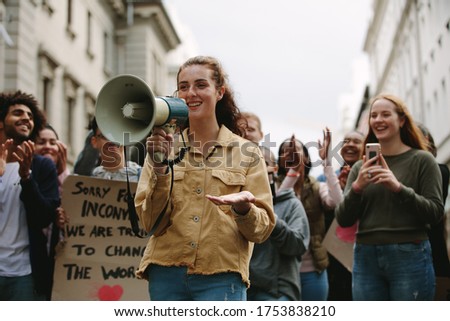 Woman with a megaphone in a rally outdoors on road. Woman standing outdoors with group of demonstrator clapping and celebrating.