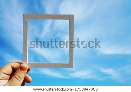 Hand holding a wooden frame on blue sunrise sky background. Care, safety, memory or painting concept.                       
