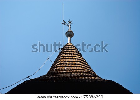 Old iron weathercock at the top of an old village belltower on summer blue sky