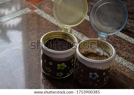 Stock photo of two flower design printed glass jar or container with plastic cap full with cumin seed and mustered seed. Picture captured under bright light at Bangalore, karnataka, India.