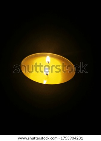 Lit candle with two wicks creating a bright yellow soothing and warm light on a very dark background.