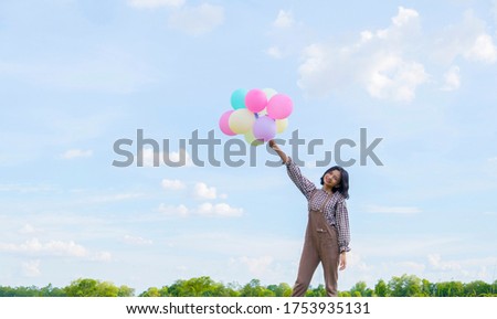 Asian girl holding colorful balloons with blue sky background.