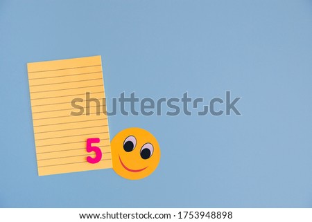 A lined yellow Notepad with the number five at the bottom and a smiling yellow smiley face on a blue background. Flat layout with copy space