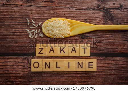 Conceptual zakat (islamic tax) with rice. Obligation to aid the poors. ZAKAT ONLINE text on wooden table. Islamic zakat (islamic tax) concept. Selective focus.