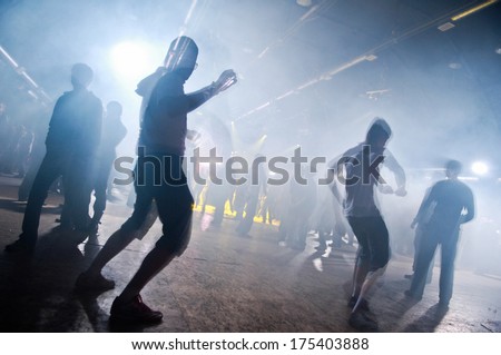 Picture of a lot of people enjoying night perfomance of famous dj, large crowd of youth dancing with raised up hands on rock concert, party in dance club, bright yellow light from stage, nightlife