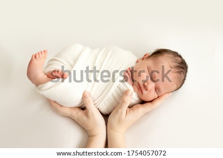 a newborn baby sleeps sweetly in his mother's arms on a white background, swaddling the baby, a place for text. Royalty-Free Stock Photo #1754057072