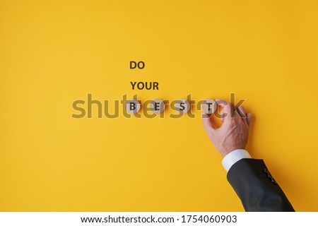 Hand of a businessman making a Do your best sign spelled on yellow background and wooden cut circles. 