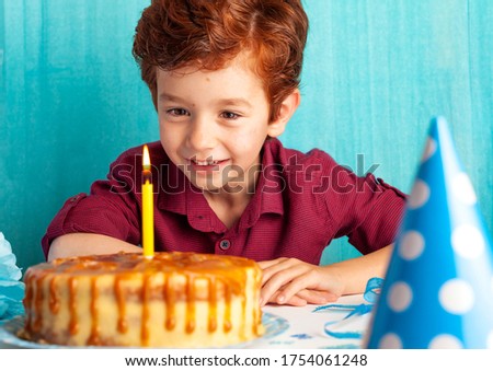 happy child, boy looks at a cake with a candle on a blue background