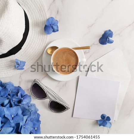 Cup of coffee, blue hydrangea flower, sunglasses, summer hat and empty card with envelope on marble background. Birthday, morning coffee, summer vacation, blue monday concept.  Top view. 