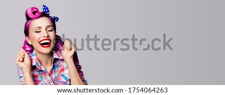 Unbelievable news! Excited surprised, very happy purple woman. Pin up girl with open mouth, closed eyes and raised hands. Retro and vintage. Grey color background. Wide composition picture, copy space