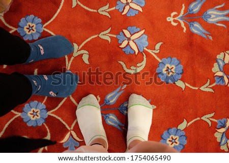Photo of two people wearing socks standing in red prayer carpet with flower design of the Blue Mosque in Istanbul Turkey
