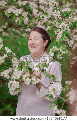 Elderly brunette woman in white clothes posing in the apple orchard with blooming apple branches