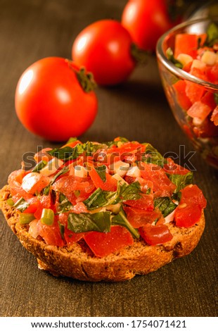 Vertical still life shot of a  round craft buns bruschetta and three red tomatoes and glass bowl close-up on a wooden textured table
