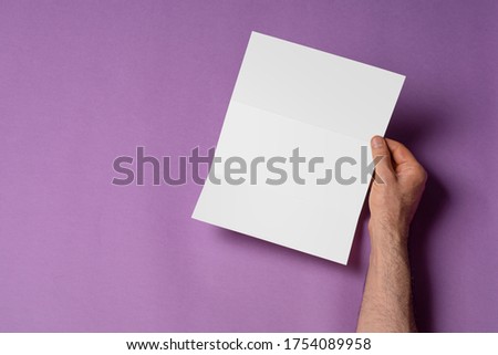 Male hands holding a tri-fold brochure with blank pages on purple background, mock-up series template ready for your design, selection path included
