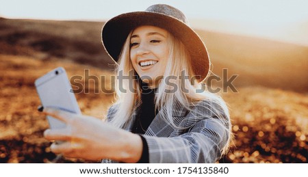 Gorgeous blonde caucasian lady with nice hat making a selfie while smiling a sunny field