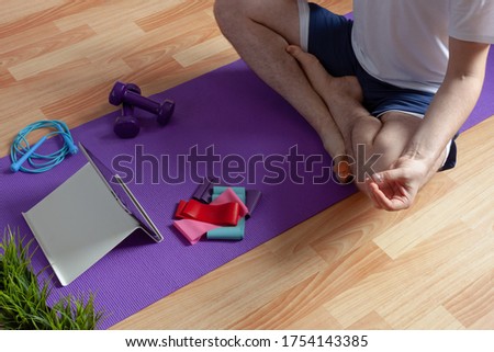 a young man is engaged in fitness at home online lessons, near sports equipment dumbbells, elastic bands