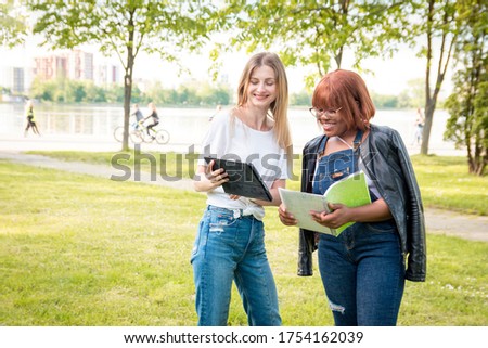 Two female students communicate in the park. Cheerful conversation riznonatsionalnyh girls