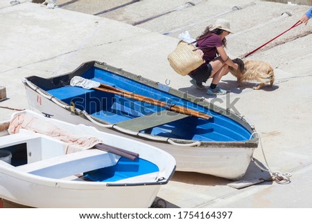 Summer wanderlust of a woman enjoying on the beach in Majorca, the girl has long hair and wears a hat and sunglasses, the woman holds a beach bag or typical Mallorcan basket and play with a dog