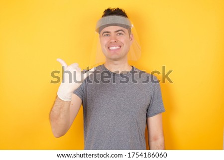 Young caucasian man wearing t-shirt and face shield standing over isolated yellow background showing up number six Liu with fingers gesture in sign Chinese language