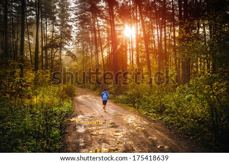 Jogger running a muddy path in autumn forrest with sun rising up