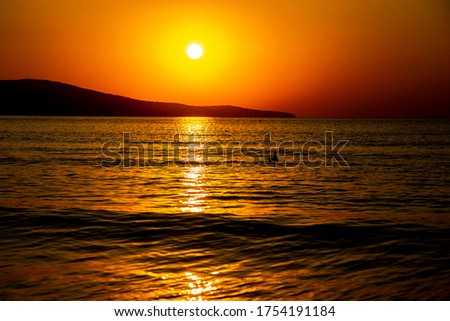 Beautiful orange view at sunrise, of the calm sea and sea coast with hills in the distance