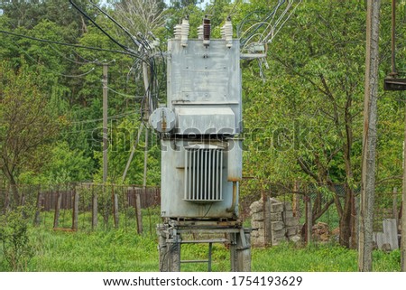 one gray large iron transformer with electrical wires stands on the street against a background of green vegetation