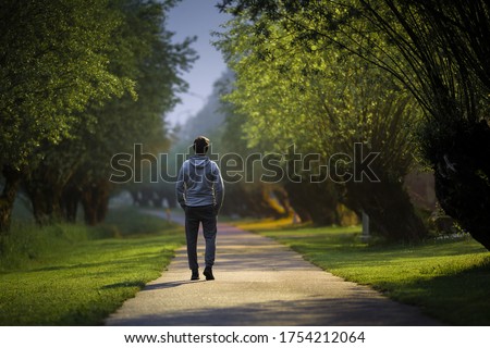 Young alone man slowly walking through alley of trees in warm summer night. Spending time alone in nature. Peaceful atmosphere. Back view. Royalty-Free Stock Photo #1754212064