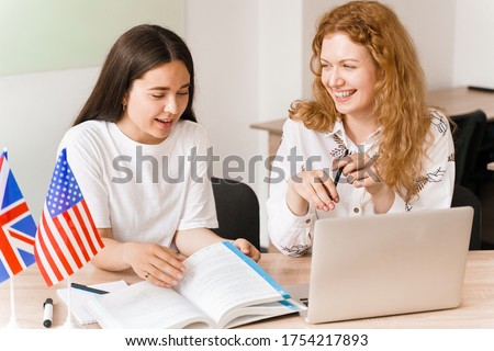 Foreign school private study, smile, laught with a school girl. Teacher explain grammar of native language using laptop. Prepearing to exam with tutor. English and British flags in front. Royalty-Free Stock Photo #1754217893