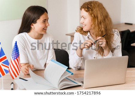 Foreign school private study, smile, laught with a school girl. Teacher explain grammar of native language using laptop. Prepearing to exam with tutor. English and British flags in front.