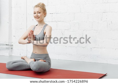 Gorgeous young female wearing her sportswear, holding hands in namaste or prayer, keeping eyes closed while practising yoga and meditating at home alone, having calm look on her face