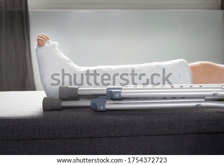 Detail left leg or in white plaster placed on a gray sofa or stool.Broken leg in plaster. The boy has a broken ankle. Royalty-Free Stock Photo #1754372723