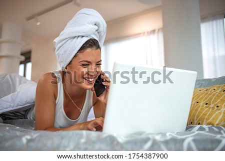 Happy at home. Woman using smartphone while lying in bed and having rest. Morning work. Middle age business woman. Girl is talking in the morning and browsing with her laptop 