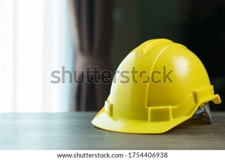 Yellow helmet, safety hat on brown wooden table.