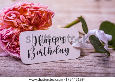 Birthday background with flowers and card. Rose and happy birthday word on white card. Pastel colors on selective focus image.