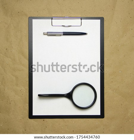 A tablet with a white sheet of A4 format with magnifier, pen and magnifier on a beige craft paper. Concept of analysis, study, attentive work. Stock photo with empty place for your text and design.