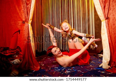 Family during a stylized theatrical circus photoshoot in a beautiful red location. Models mother and daughter posing on stage with curtains